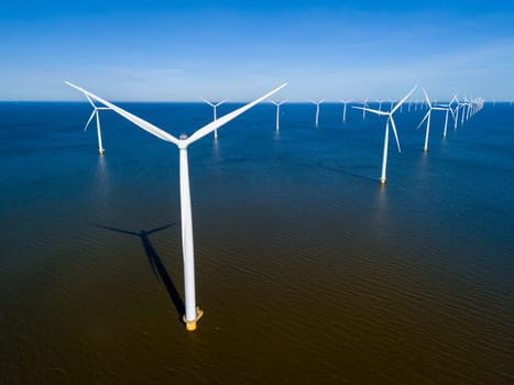 A cluster of wind turbines stands tall in the ocean, the power of the wind as they rotate against the backdrop of the spring sky. drone aerial view of windmill turbines green energy in the ocean