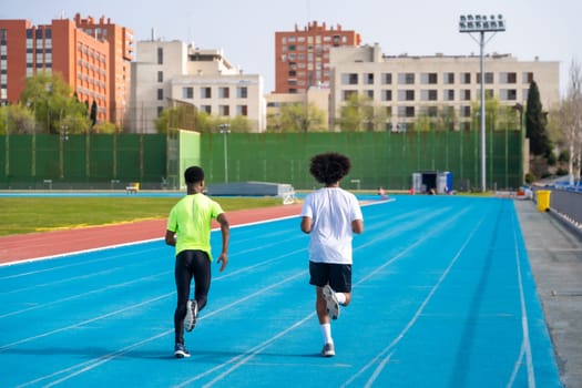 Full length rear view of two sportive african men running in an athletics track
