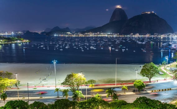 Vibrant night bay with boats and illuminated city against a hill.