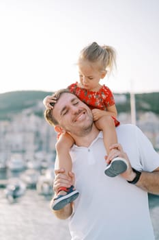 Little girl examines her father face while sitting on his shoulders and holding his head. High quality photo