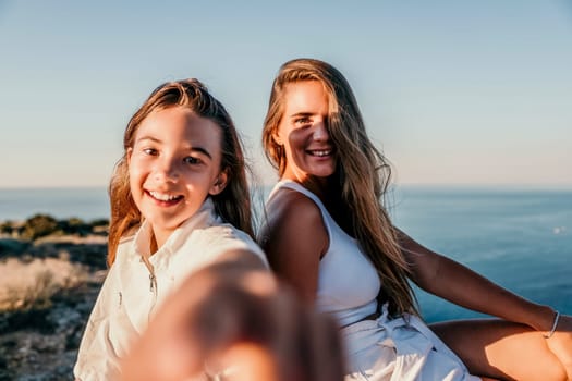 Close up portrait of mom and her teenage daughter hugging and smiling together over sunset sea view. Beautiful woman relaxing with her child.