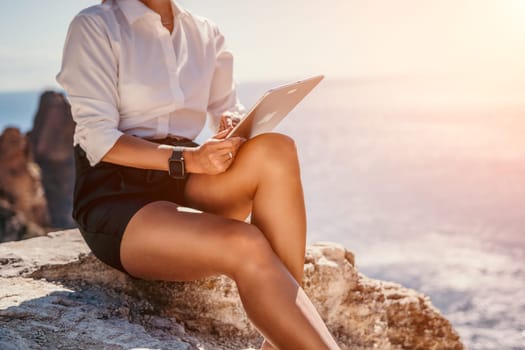 Successful business woman in yellow hat working on laptop by the sea. Pretty lady typing on computer at summer day outdoors. Freelance, travel and holidays concept.