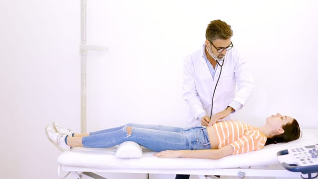 Male doctor auscultating the patient's abdomen with a stethoscope in a clinic