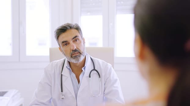 Mature male doctor listening to a female patient in a clinic