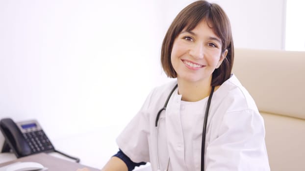 Female doctor using computer and smiling at camera in a clinic