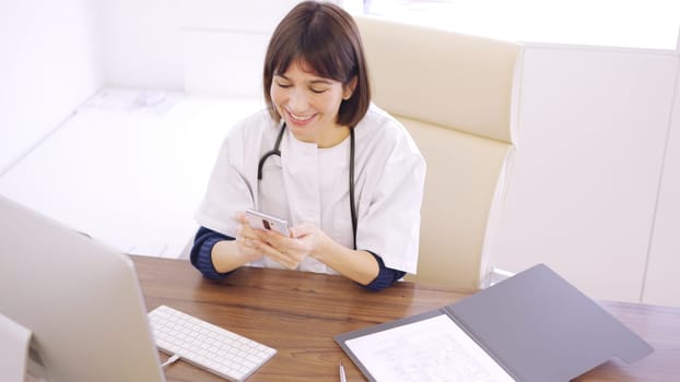 Female doctor in her office looking at her cell phone smiling