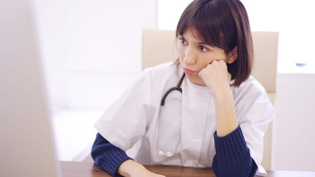 Worried female doctor looking at the screen of a computer sitting on a desk in the clinic