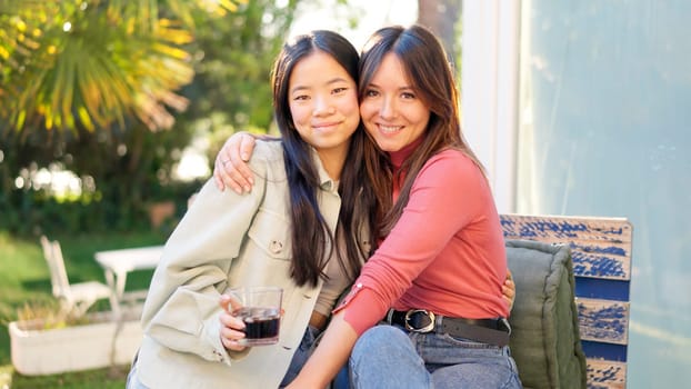 Two multiracial best friends smiling at camera while chilling in the garden during sunset