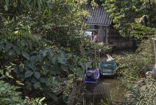 Wooden rowboat and Small motor boat moored behind house on canal amongst trees and water. Space for text, Selective focus.