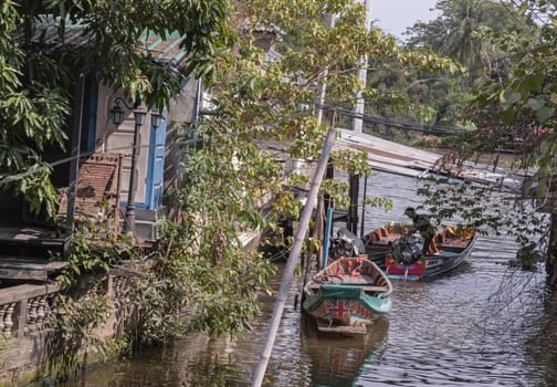 One wooden rowboat and Two small motor boat moored behind house on canal amongst trees and water. Space for text, Selective focus.