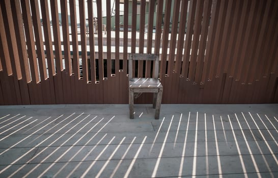 The old wooden chair is in front of the wall, which the sunlight is through it. Relaxing corner in the sunny day with good atmosphere, Space for text, Selective focus.