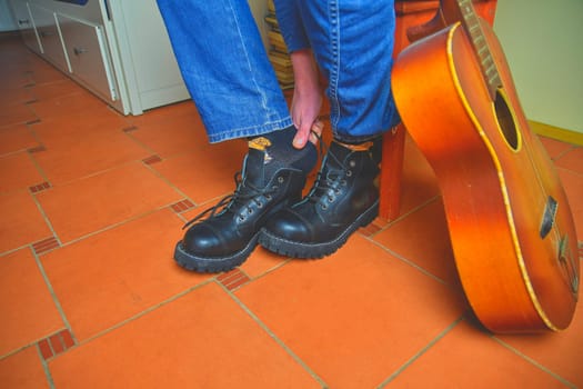 Rock and roll concept. Black boots and acoustic guitar. Putting on rock and roll boots.