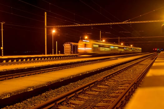 High speed passenger train on tracks with motion blur effect at night. Railway station in the Czech Republic.