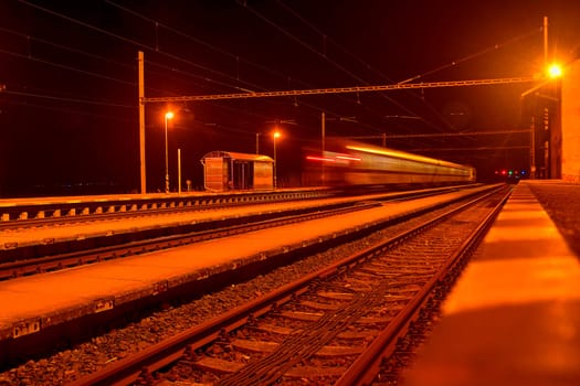 High speed passenger train on tracks with motion blur effect at night. Railway station in the Czech Republic.