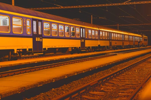 White and blue train standing at a small roofless train station at night in the Czech Republic. European train.