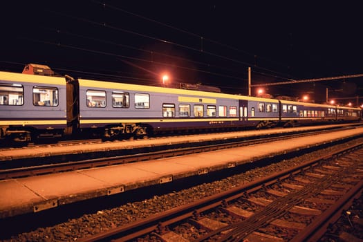 White and blue train standing at a small roofless train station at night in the Czech Republic. European train.