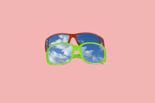 Top view of sunglasses on pastel pink background. Blue skies reflecting in sunglasses. Copy space. Minimalism design.