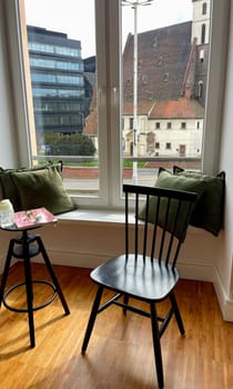 a wooden chair in front of a window with a view of the city, as part of the interior.