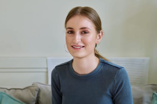 Portrait of beautiful happy smiling teenage girl looking at camera, sitting on couch at home. Age 16,17,18 years, lifestyle, youth concept