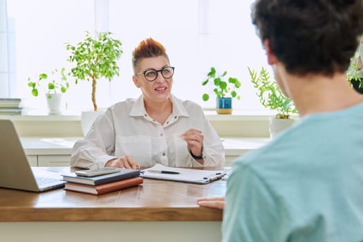 Middle-aged female professional psychologist mental therapist talking with young man in office. Psychotherapist advisor working with male patient. Psychology psychotherapy support treatment assistance
