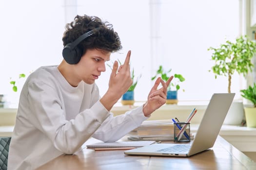 Young guy college student in headphones looking at web cam computer laptop, talking, studying online, sitting at home at desk. E-learning, remote training, education, youth, technology concept