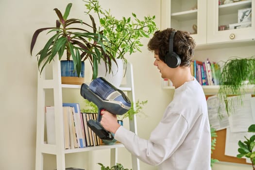 Young man wearing headphones vacuums bookshelves at home. Cleaning, hygiene, housekeeping, housework, housecleaning, youth concept