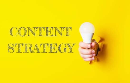 A person holding a light bulb with the word content strategy written in the background. Concept of creating and managing content for a specific purpose or goal