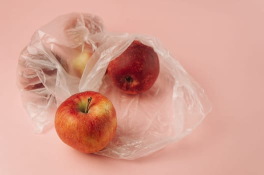 Three apples are in plastic bags on a pink background. The apples are red and shiny. The bags are clear and see-through