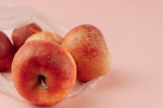 A bag of apples sits on a pink background. The apples are red and shiny. The bag is white and plastic