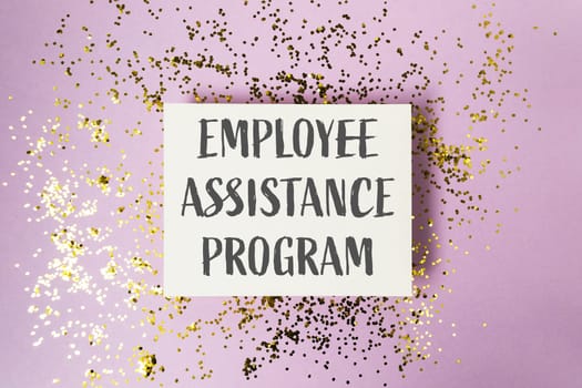 A white sign with gold glitter on it that says Employee Assistance Program. The sign is on top of a purple background