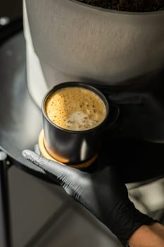 Close-up of a human hands in black gloves holding and showing a cup with a hot drink. The doctor poured coffee from the coffee machine