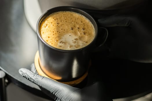 Close-up of a human hands in black gloves holding and showing a cup with a hot drink. The doctor poured coffee from the coffee machine