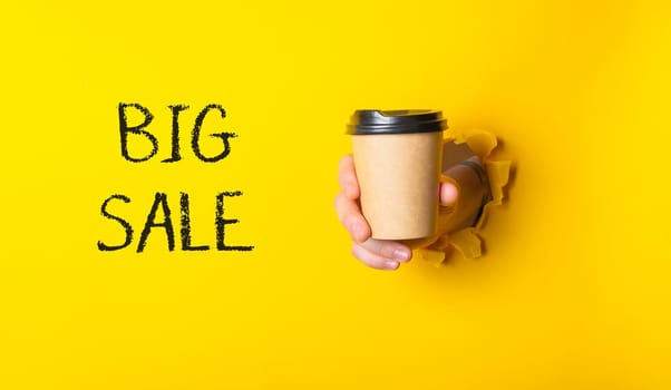 A person is holding a coffee cup with the words Big Sale written on it. The image has a yellow background and a black and white coffee cup