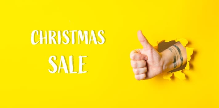 A hand giving a thumbs up with the words Christmas Sale written below it. The image has a positive and festive mood, as it is a thumbs up gesture