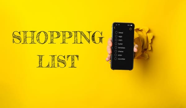 A person holds a cell phone displaying a shopping list, reflecting modern convenience and digital organization for everyday tasks like grocery shopping.
