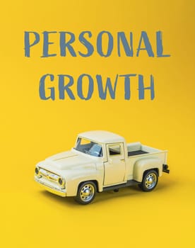 A toy truck is on a yellow background with the words Personal Growth written below it. Concept of personal growth and development, as the toy truck represents a journey or progress towards a goal