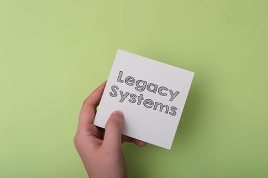 A hand holding a piece of paper with the word Legacy Systems written on it. Concept of passing down knowledge and traditions from one generation to the next