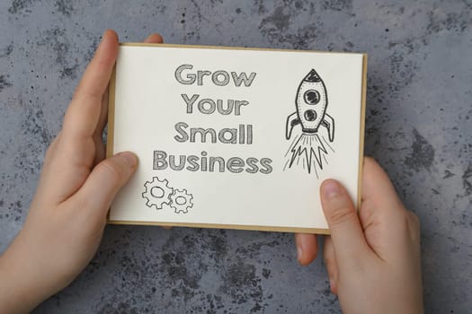 A hand holding a piece of paper with the words grow your small business written on it