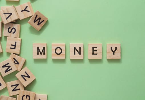 A jumble of wooden letters spell out the word money. The letters are scattered across the image, with some overlapping and others standing alone. Scene is one of confusion and disarray