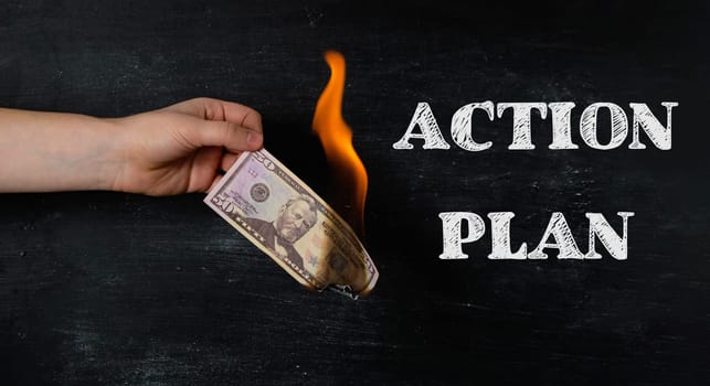 A hand holding a burnt dollar bill with the words Action Plan written below it. Concept of taking action and making a plan to achieve a goal