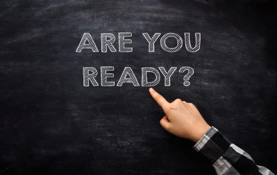 A hand pointing at a chalkboard with the words Are you ready written below it, illustrating a business concept.