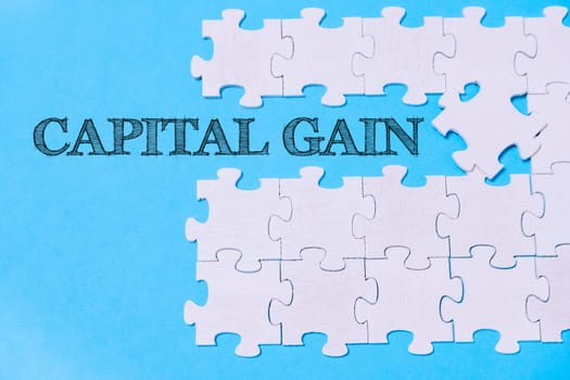 A jigsaw puzzle with the word Capital Gain written on it. The puzzle pieces are scattered across the image, creating a sense of disarray and uncertainty. The blue background adds a sense of calmness