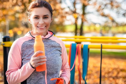 Fitness girl with bottle with water after exercising in autumn park outdoors. Young woman and hydration sport portrait at fall season