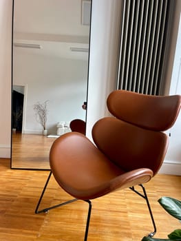 A brown leather chair and a large mirror as part of the decor in the interior of the room. High quality photo