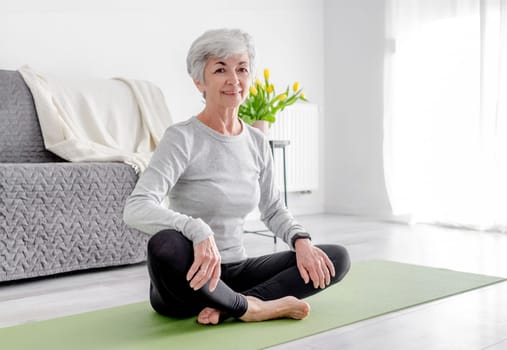 Sweet Woman Looks Into Camera While Sitting On Yoga Mat, Embodying Active Lifestyle, Practicing At Home