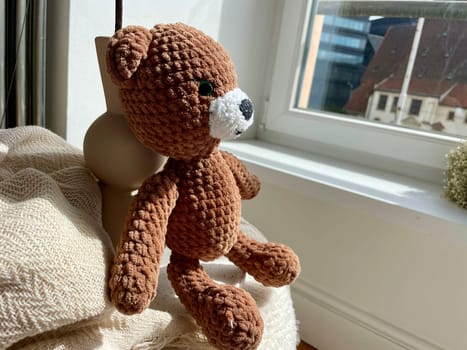 Children's toy of a knitted brown bear looking out the window. High quality photo