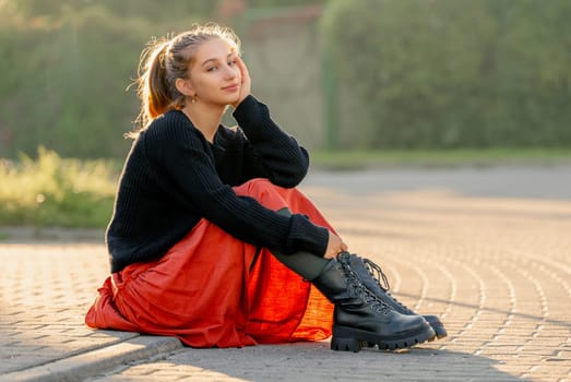 Beautiful teenager girl in red skirt sitting outdoors at street. Pretty teen model posing in trendy clothes