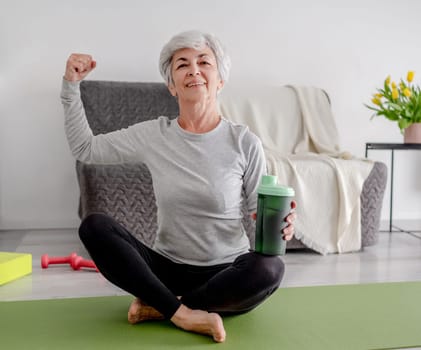 Cheerful Elderly Woman Looks Into The Camera And Shows Off Her Bicep, Embodying An Active Lifestyle And Home Workouts