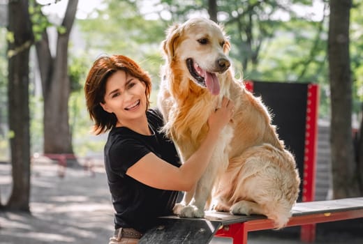 Girl petting golden retriever dog after training and smiling outdoors. Young woman with doggy petportrait in the park together