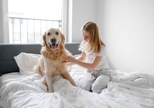 Girl Plays With Golden Retriever In Bed In The Morning In A Bright Room